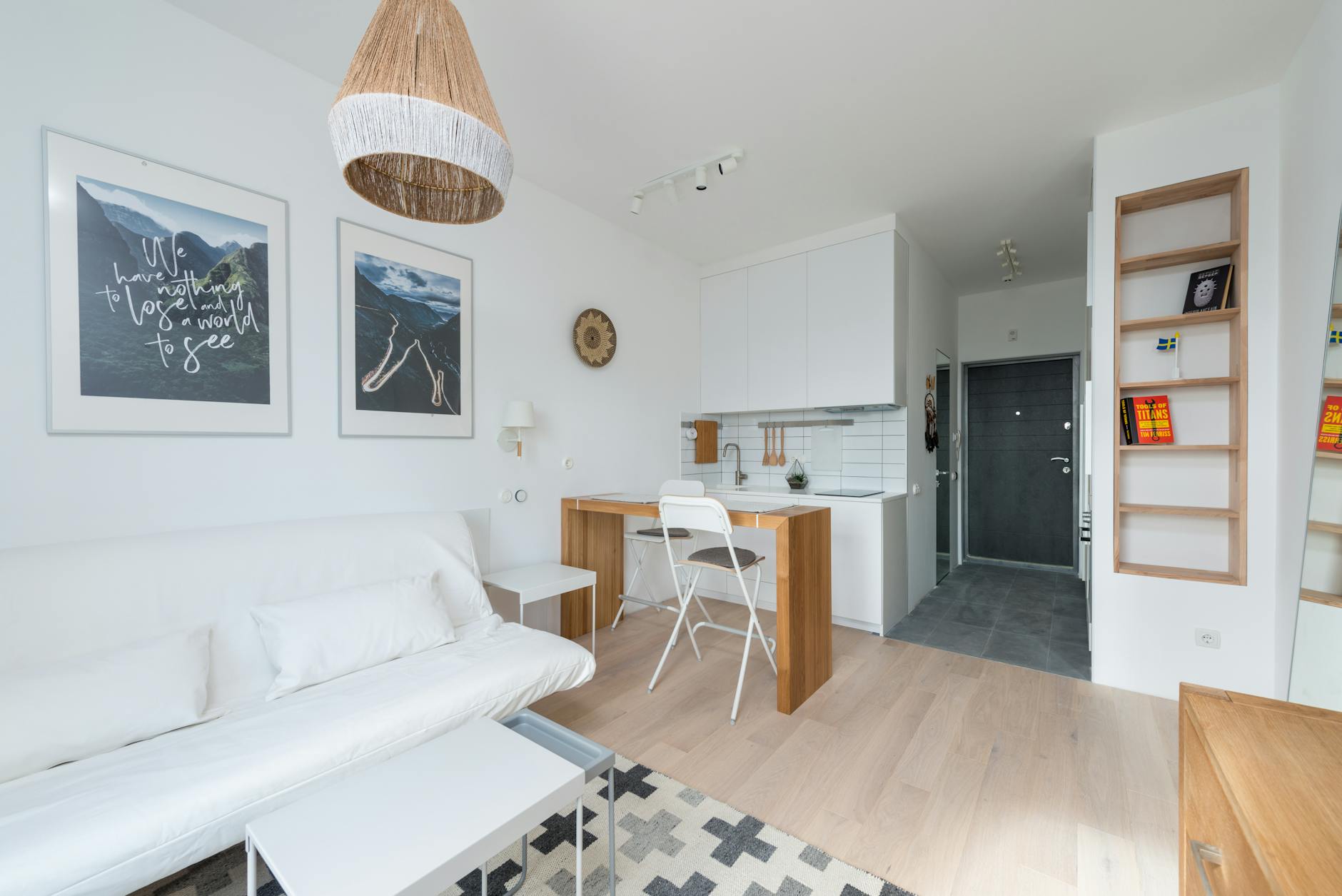 A bright small apartment with a white sofa, wooden table, and open kitchen