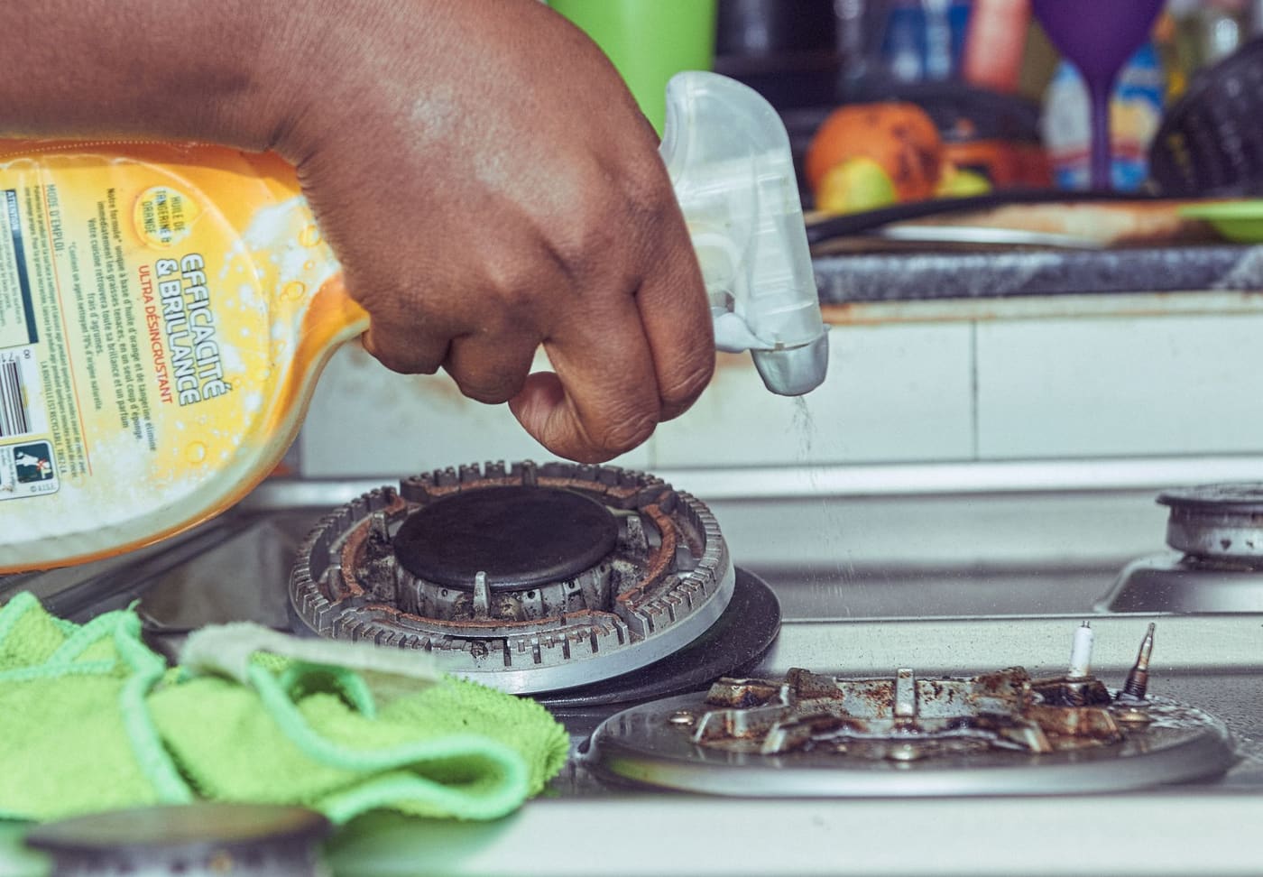 A hand wiping a gas stovetop with a cloth and spray cleaner