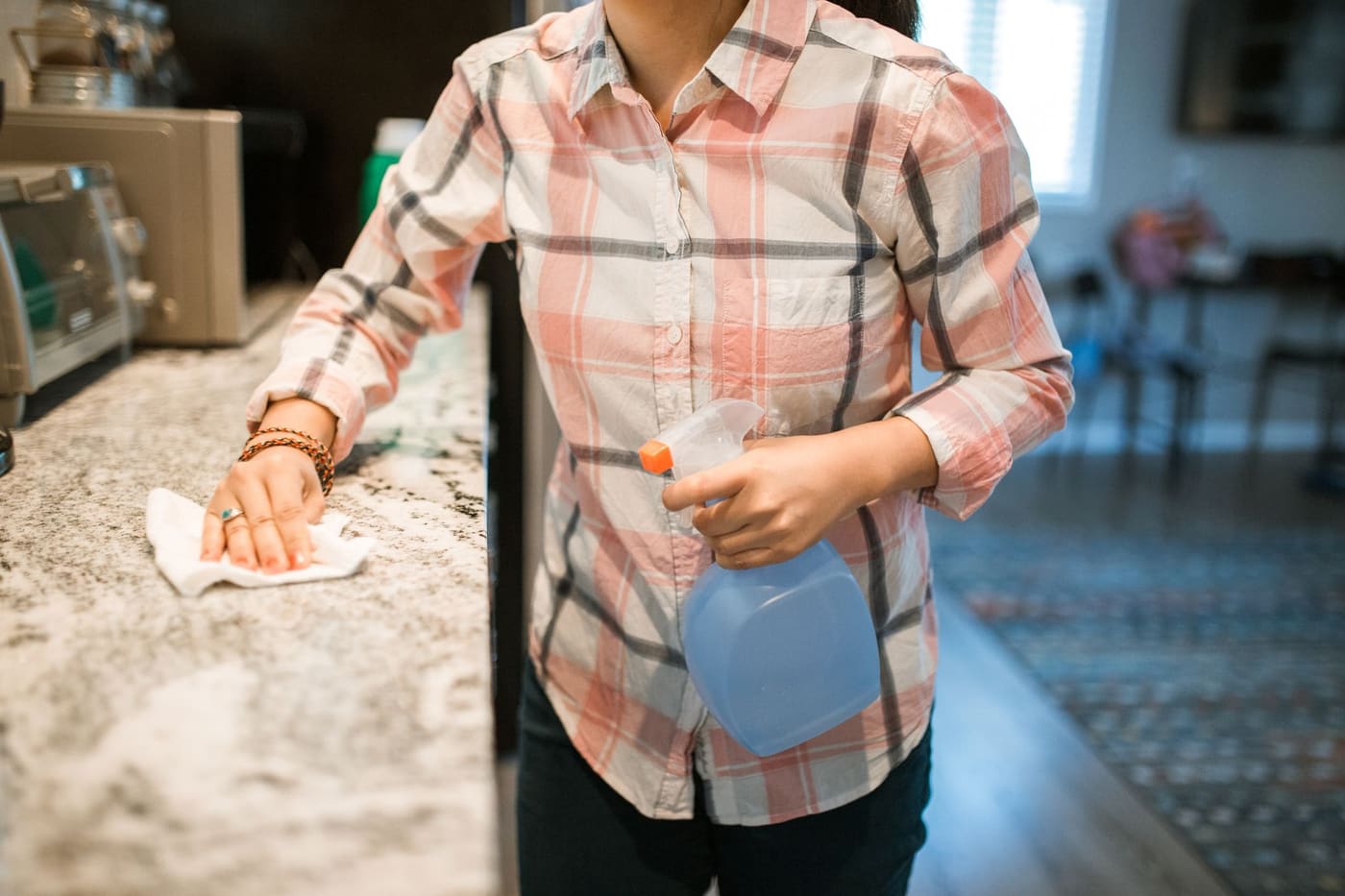 A person wiping a kitchen counter with a spray bottle and cloth