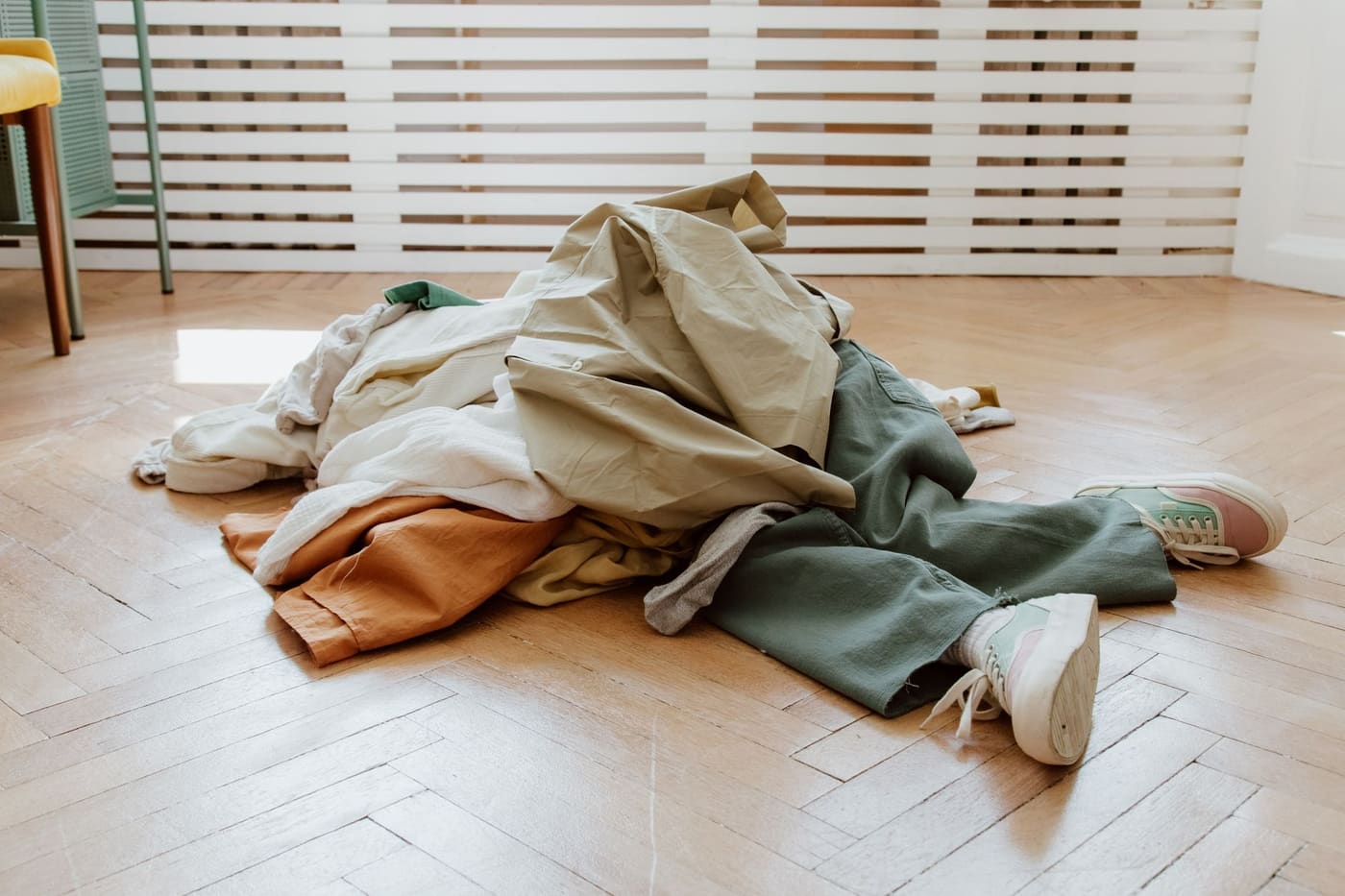 A pile of clothes on a wooden floor in a bright, nearly empty room
