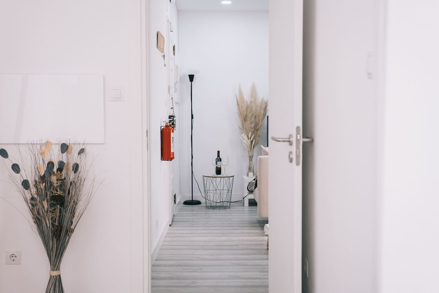 A white hallway with dried grass stems in vases and a simple floor lamp