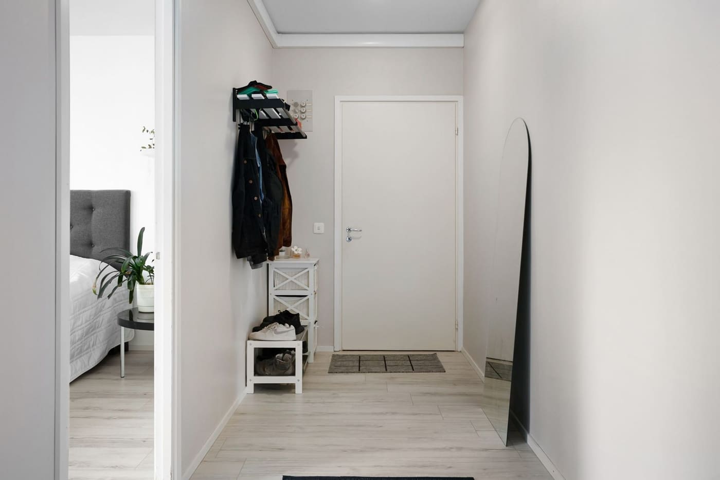 A narrow apartment entry with coat hooks, a small bench, and a shoe mat by the door