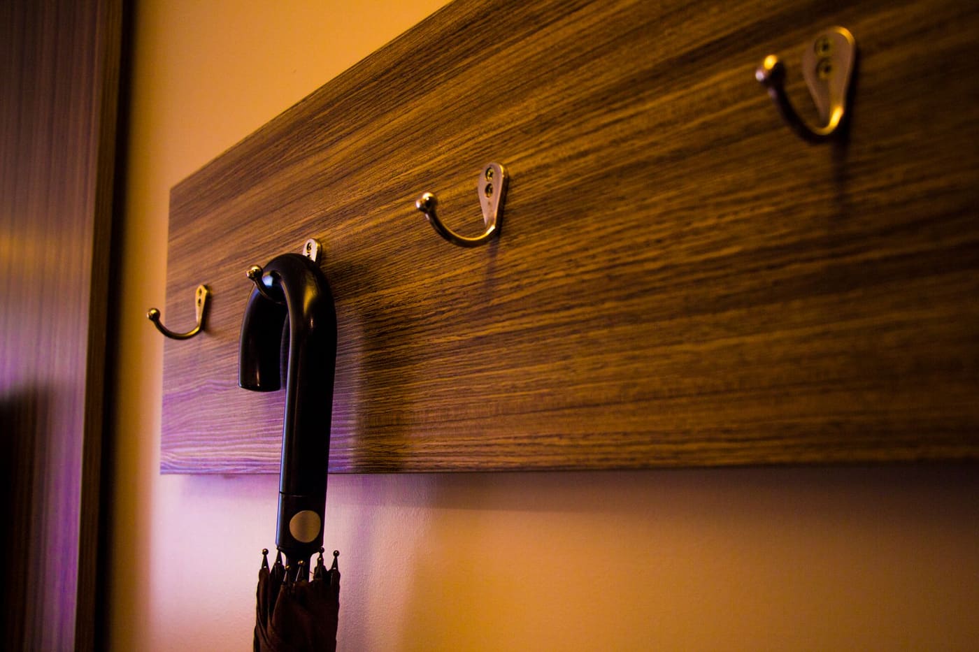 A wooden hook board on a wall with a black umbrella hanging from one hook
