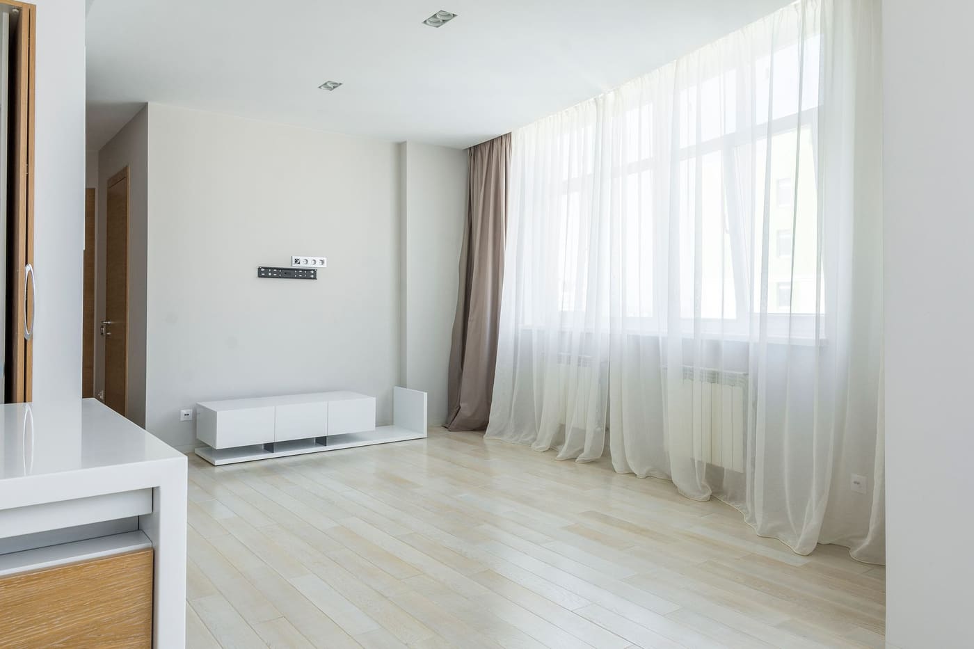 Sheer white curtains hung wide across tall windows in a pale living room with a light wood floor