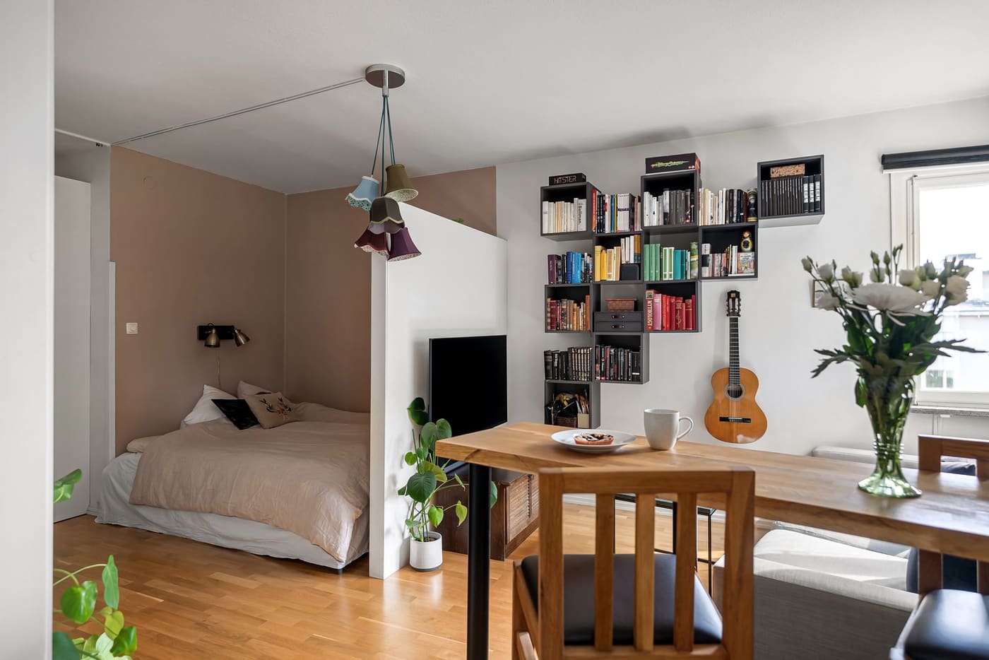 A small studio apartment with a made bed, a bookshelf, and soft lighting