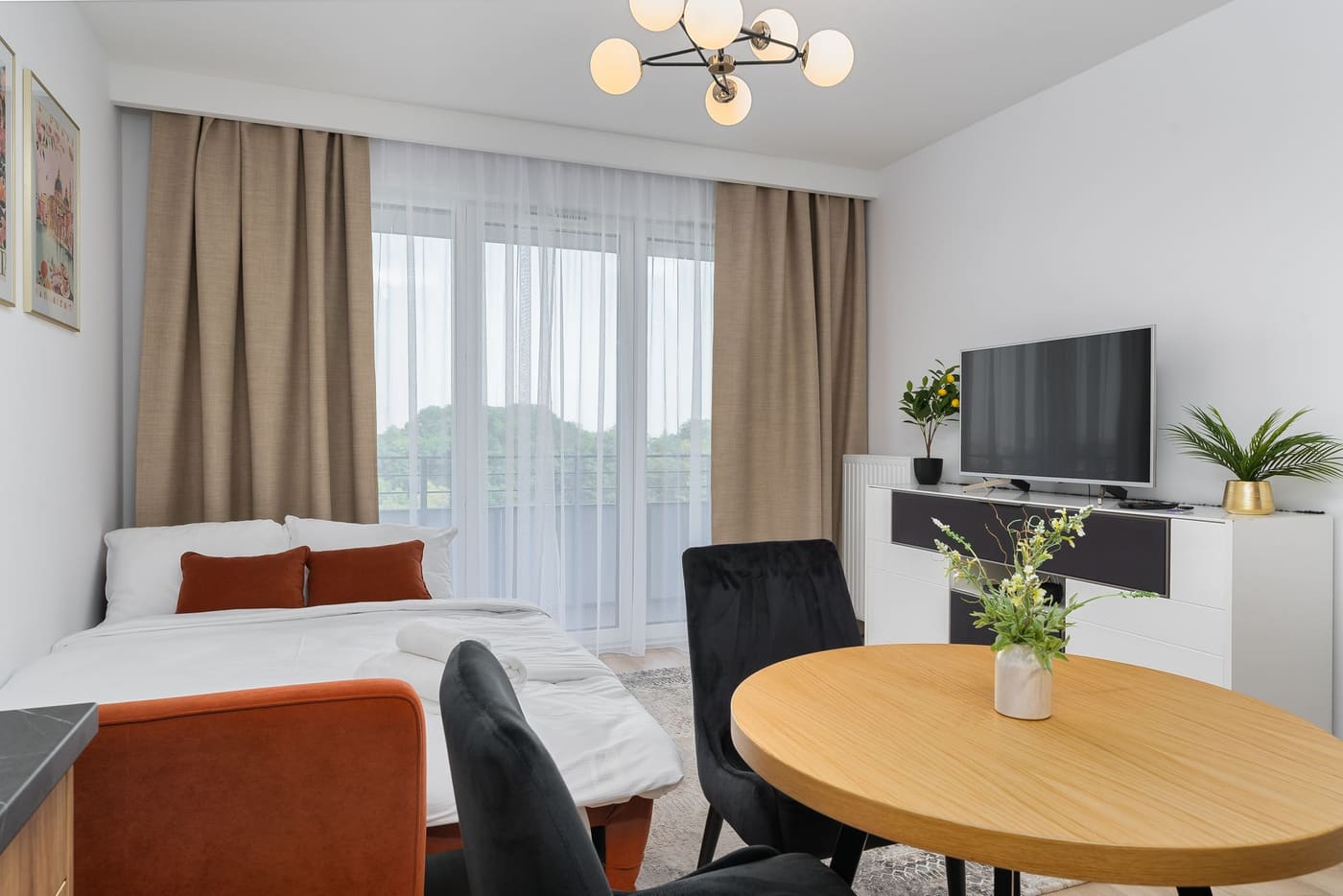 A small studio apartment with a bed, a sofa, and a round table by a window