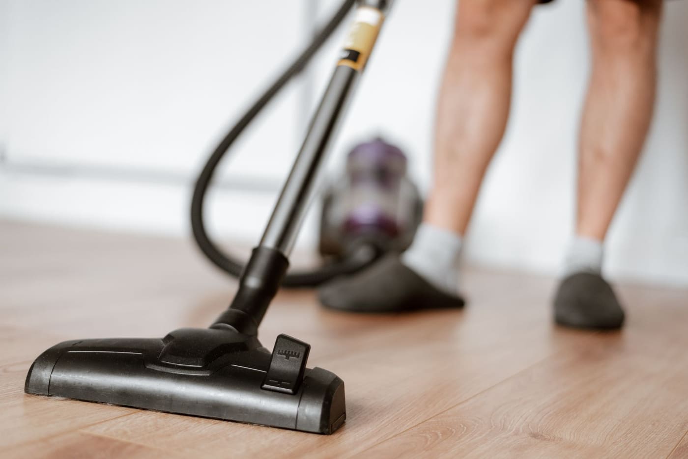 A vacuum cleaner head on a wooden floor with a person's slippered feet nearby